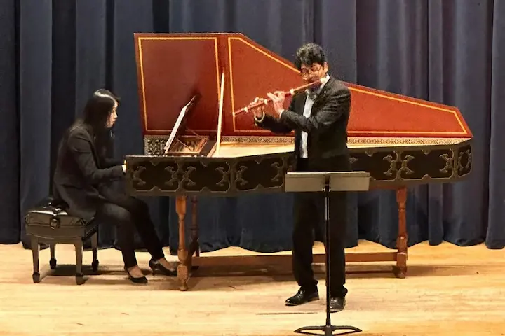 A traverso player and harpsichordist playing together in a recital hall